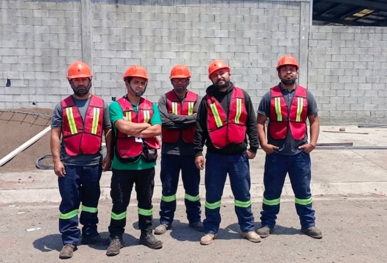 Cinco trabajadores de construcción con equipo de seguridad de pie en línea en un sitio de trabajo