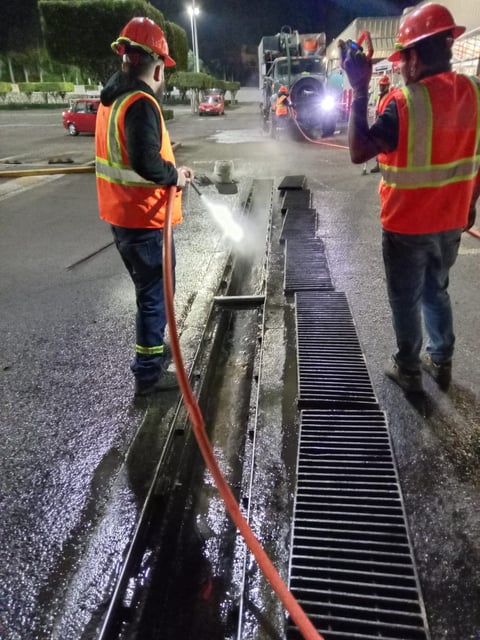Trabajadores limpiando canal de drenaje nocturno con manguera